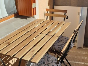 Une table en bois, accompagnée d’un banc, d’une chaise et d’un coussin à motifs.