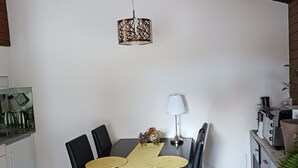 Comedor con una mesa preparada para cuatro personas, lámpara colgante y zona de cocina con electrodomésticos.