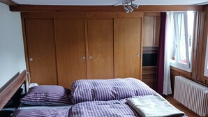 Una habitación con cama, armario de madera y ventana con cortinas.