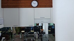 Una cocina con armarios blancos, un lavamanos de acero inoxidable y un techo de madera con un reloj.
