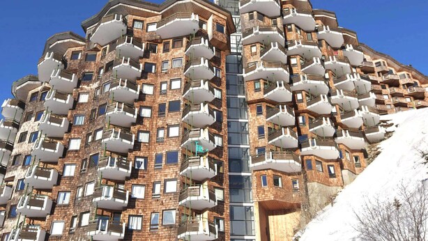 Un edificio residencial de varios pisos, con balcones, una escalera central y una pendiente nevada a la derecha.