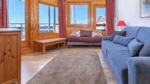 Una habitación acogedora con paredes de madera, una cama, un sofá y vistas a un paisaje nevado a través de amplias ventanas.