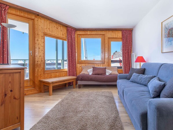 Una habitación acogedora con paredes de madera, una cama, un sofá y vistas a un paisaje nevado a través de amplias ventanas.