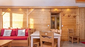 A wooden cabin interior with a dining table, chairs, a sofa with red cushions, and a mirror on the wall. - Renovated apartment for 8 in Avoriaz, mountain charm and modern (Avoriaz)