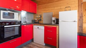 A compact kitchen with red cabinets, a white refrigerator, a microwave, a toaster, and a coffee maker. - Renovated apartment for 8 in Avoriaz, mountain charm and modern (Avoriaz)