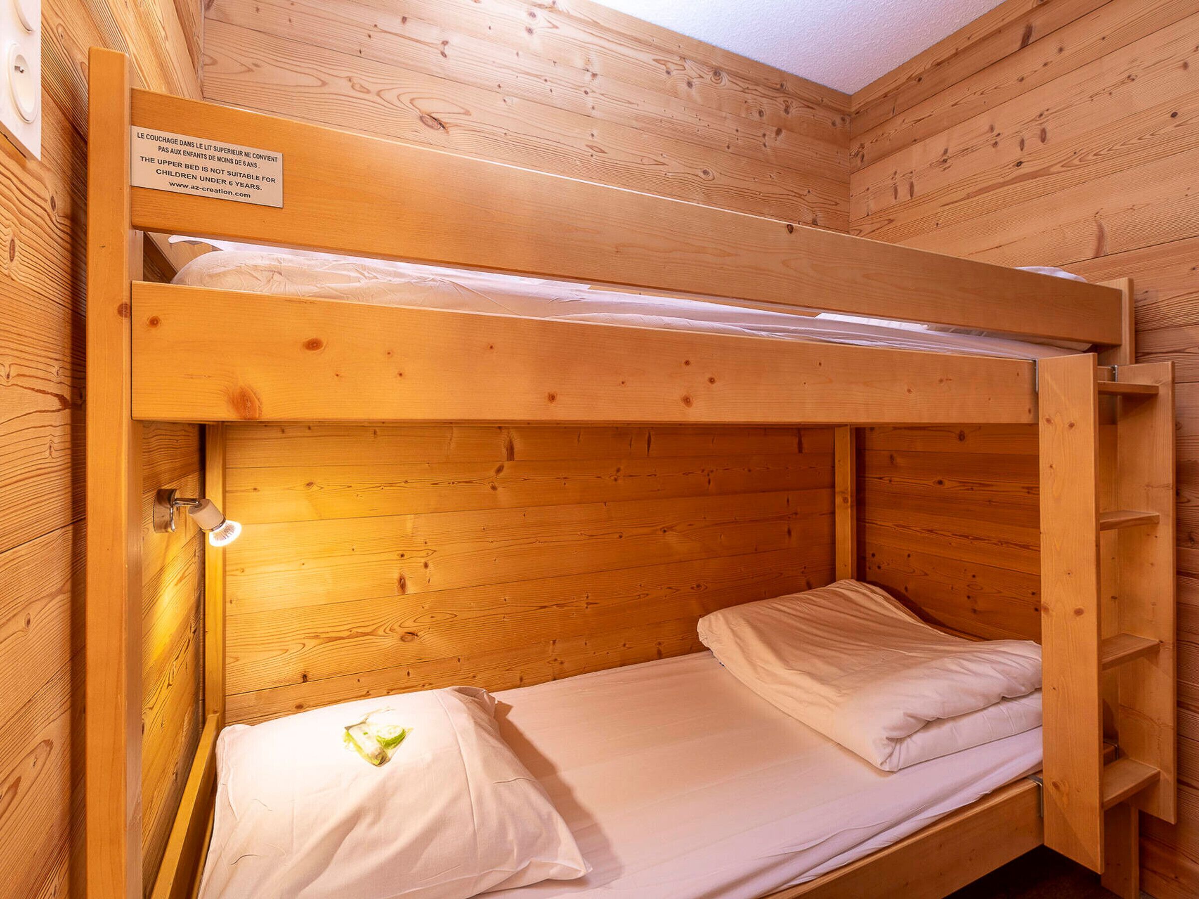 Una cama individual superpuesta con cabecera de madera y un letrero que advierte contra el uso de la cama superior para menores de 6 años.