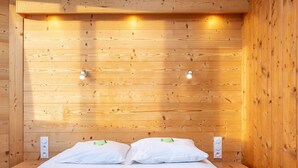 A wooden-paneled room with a bed, two bedside tables, and wall-mounted light fixtures. - Renovated apartment for 8 in Avoriaz, mountain charm and modern (Avoriaz)
