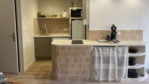 A compact kitchen with a built-in microwave, a coffee machine, and a small refrigerator.