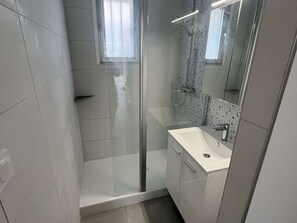 Ein modernes Badezimmer mit Duschkabine aus Glas, einem weißen Waschbecken und einem Spiegel.