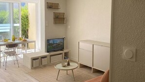 A modern living room with a TV, seating, and a view of greenery outside.