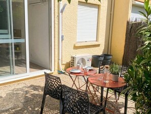A patio with outdoor furniture, a sliding glass door, a white air conditioning unit, and a window with blinds.