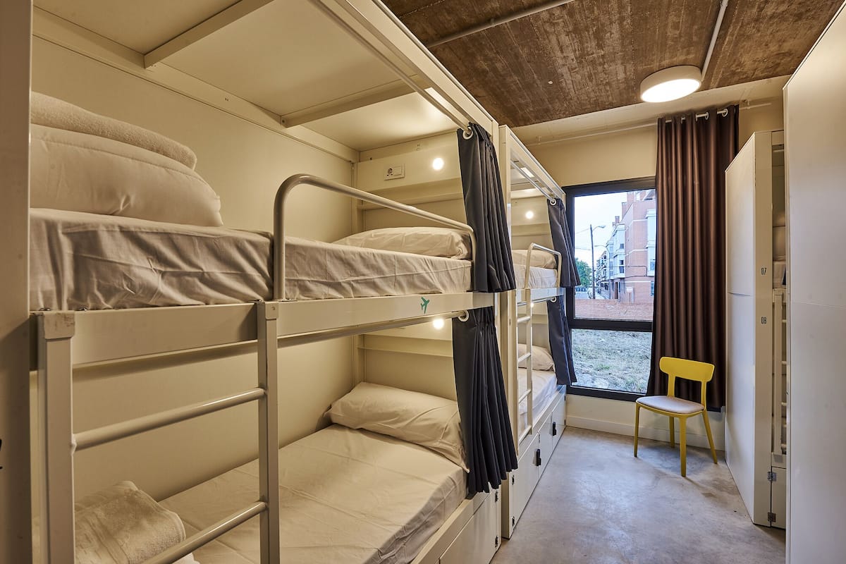 A bunk bed room with a window, a chair, and a door.