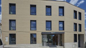 Un edificio moderno con fachada plana, múltiples ventanas y escaparate con el rótulo HOSTELFLY.