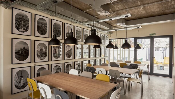 Un comedor moderno con varias mesas y sillas, fotografías en blanco y negro enmarcadas en las paredes, e iluminación colgante.