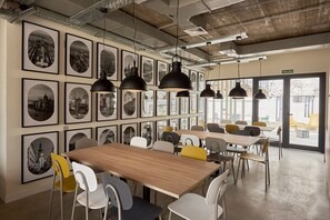 Un comedor moderno con varias mesas y sillas, fotografías en blanco y negro enmarcadas en las paredes, e iluminación colgante.