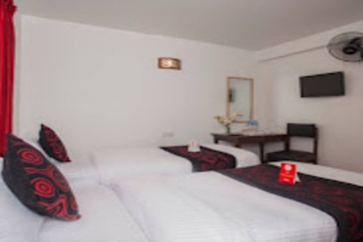 A hotel room with two beds, a desk, a chair, a TV, and a door.