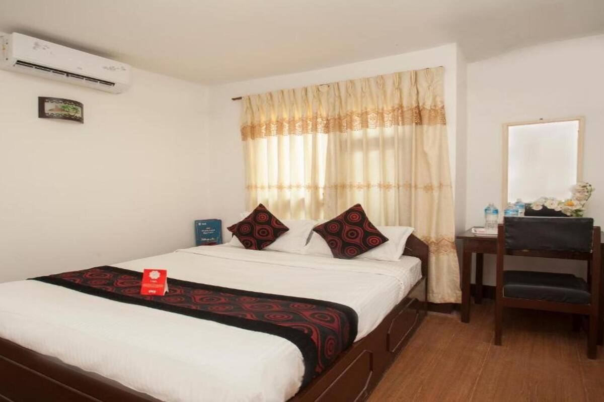 A hotel room with a bed, a desk, a chair, an air conditioning unit, and a window with curtains.