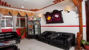 A living room with two black leather sofas, a glass cabinet with beverages, a red-framed mirror, and a window with curtains. - MeroStay 191 Hotel City Pvt. Ltd. (Kathmandu)