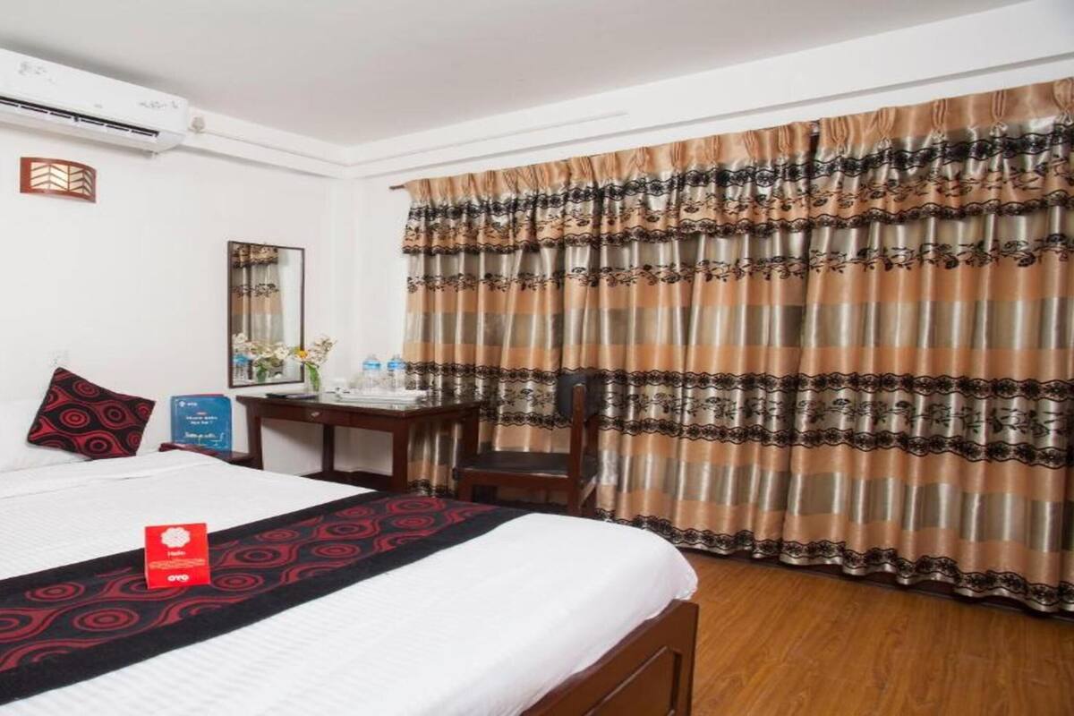 A hotel room with a bed, a desk, a chair, a mirror, and a window with curtains.