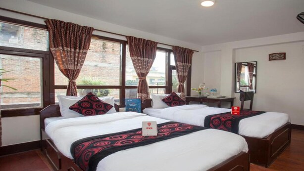 A hotel room with two beds, a desk, a chair, a mirror, and a window with curtains. - MeroStay 191 Hotel City Pvt. Ltd. (Kathmandu)