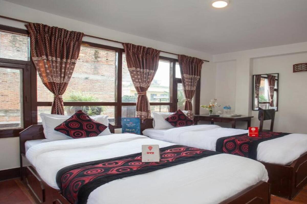 A hotel room with two beds, a desk, a chair, a mirror, and a window with curtains.