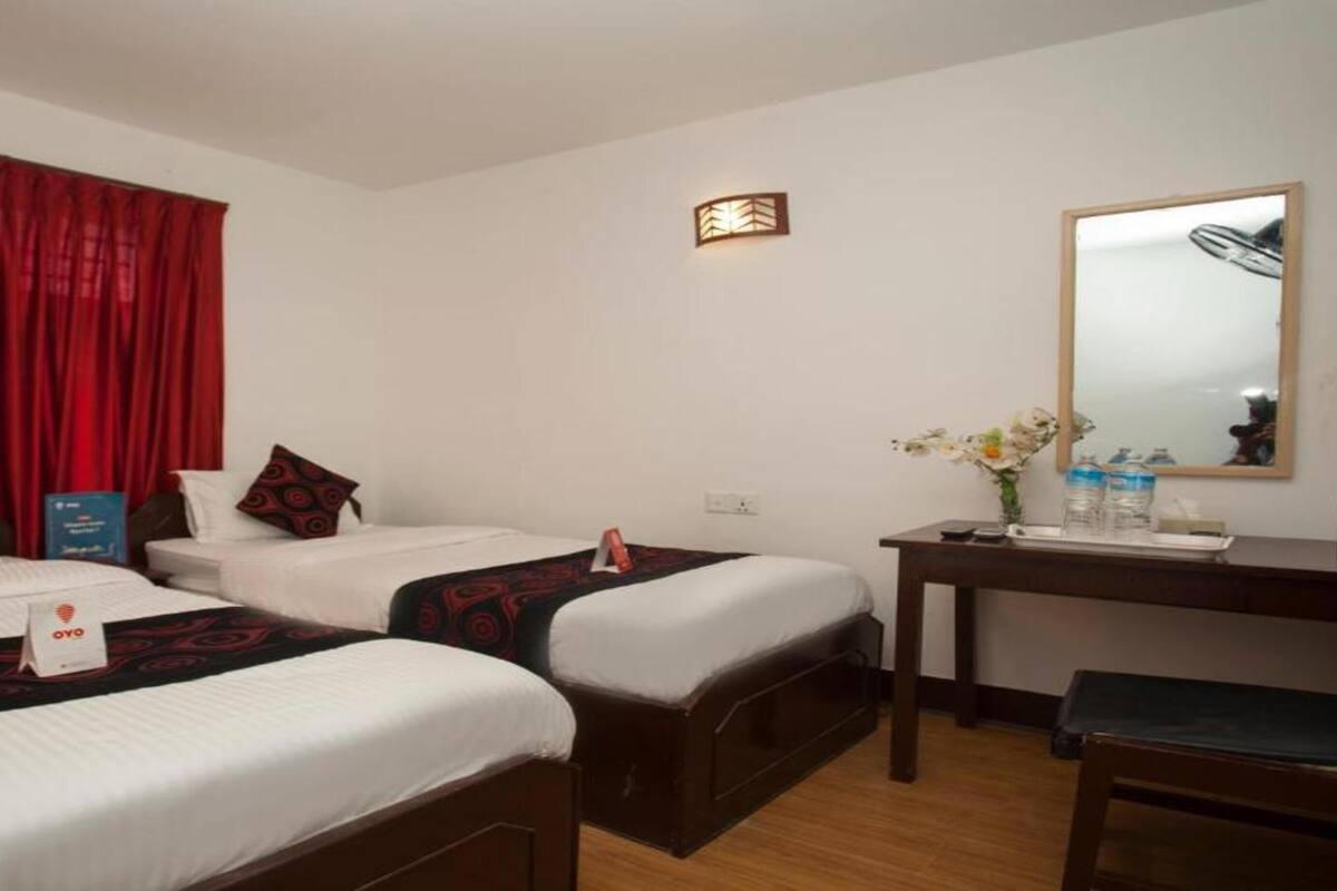 A hotel room with two beds, a desk, a chair, a mirror, and a red curtain.