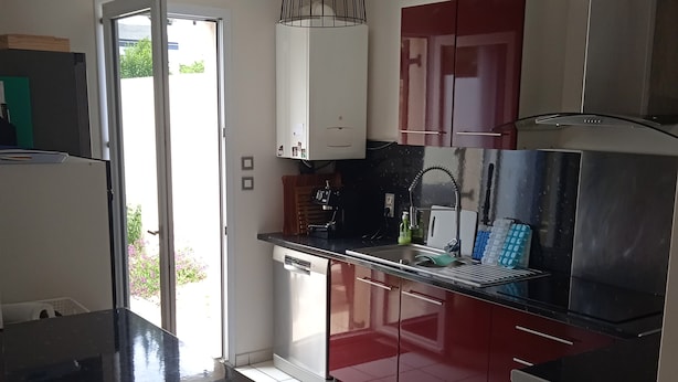 A modern kitchen with a black countertop, red cabinets, and a stainless steel range hood. - Cabellou Vras (Concarneau)
