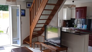 A modern kitchen with a built-in stove, a dining area with a wooden table and chairs, and a staircase leading to an upper level. - Cabellou Vras (Concarneau)