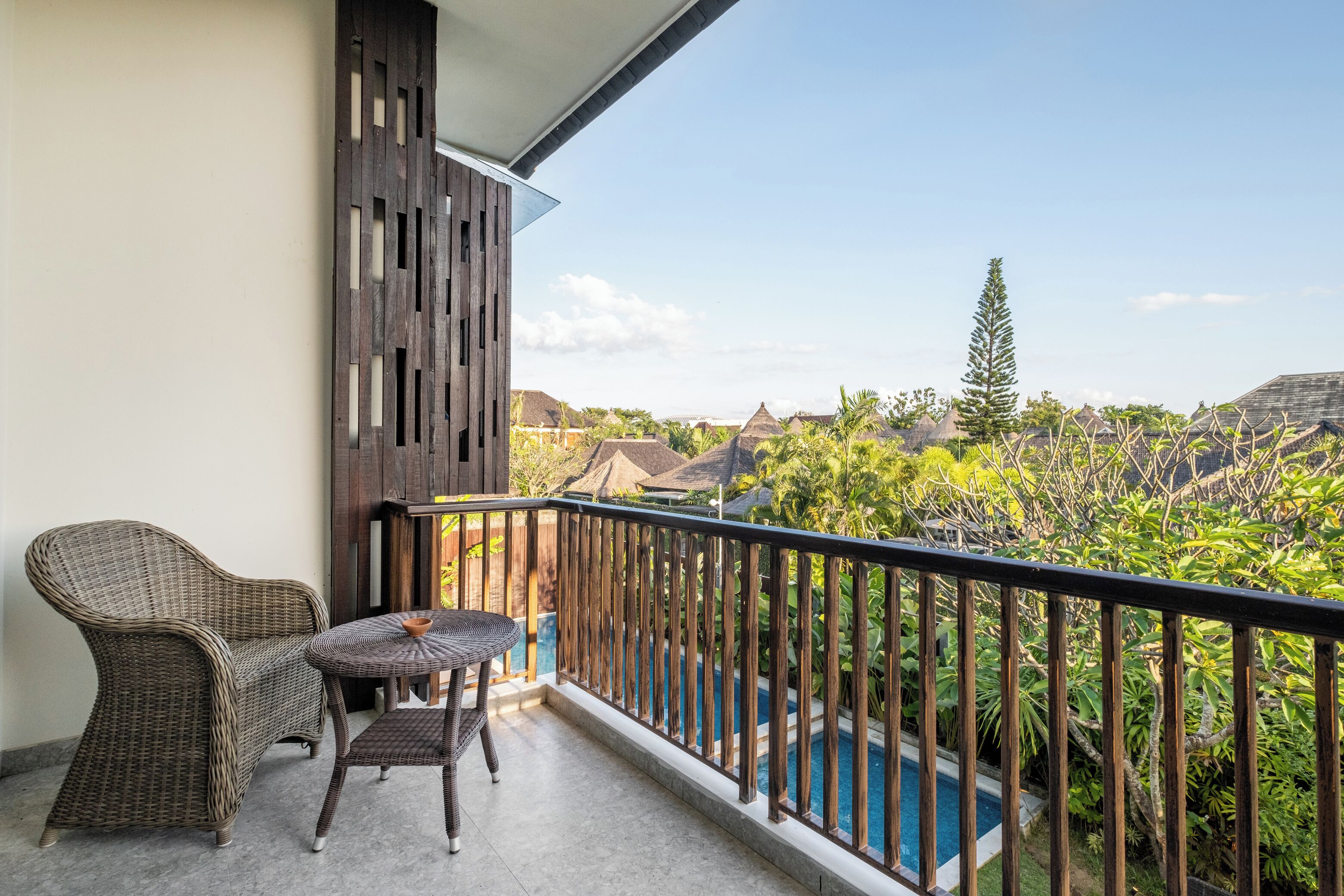 A balcony with wicker furniture, a pool, and a view of tropical vegetation.