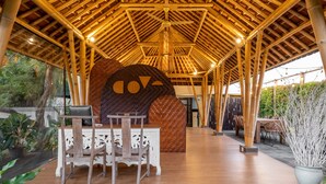 A covered outdoor area with a bamboo roof, a large decorative wall, and a dining setup with a table and chairs. - Cove Tevana (Keroboken Kelod)