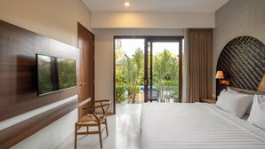 A modern hotel room with a large bed, a flat-screen TV mounted on the wall, a wooden chair, and a view of a pool and greenery outside. - Cove Tevana (Keroboken Kelod)