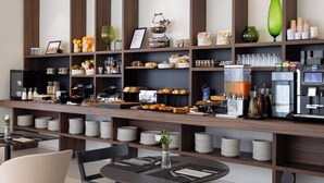 Ein Frühstücksbuffet mit verschiedenen Speisen, einer Kaffeemaschine und ordentlich angerichteten Tellern und Schüsseln.