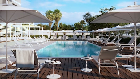 A pool area with lounge chairs and umbrellas, surrounded by greenery.
