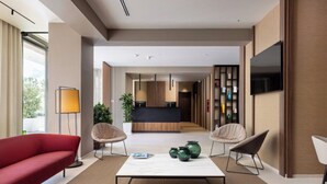 Eine moderne Hotellobby mit einem roten Sofa, zwei Sesseln, einem Couchtisch und einem an der Wand befestigten Fernseher.