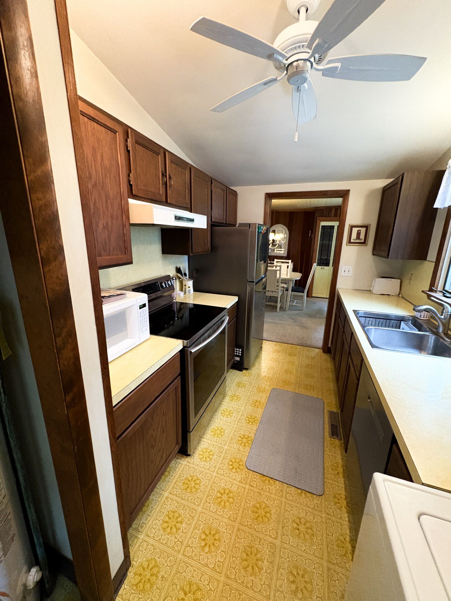 A kitchen with wooden cabinets, a microwave, stove, refrigerator, and a ceiling fan.
