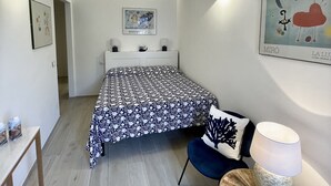 Quarto com cama, mesas de cabeceira, uma cadeira, abajur e obras de arte nas paredes.