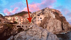 Uma cidade costeira com edifícios construídos em um penhasco, uma ponte de pedra e barcos na água.