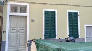 Um edifício com duas janelas com persianas verdes, uma porta branca e uma mesa de exterior coberta.