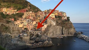 Uma cidade costeira com edifícios coloridos, uma orla rochosa e uma ponte ligando a cidade ao continente.