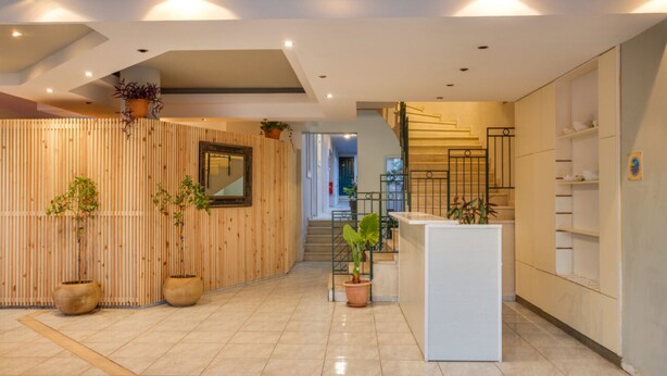 Un hall d’hôtel moderne avec un comptoir d’accueil en bois, des plantes en pot et un escalier menant aux étages supérieurs.