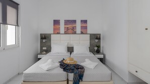 Un lit double avec une tête de lit, deux tables de chevet, une petite table et une lampe fixée au mur.