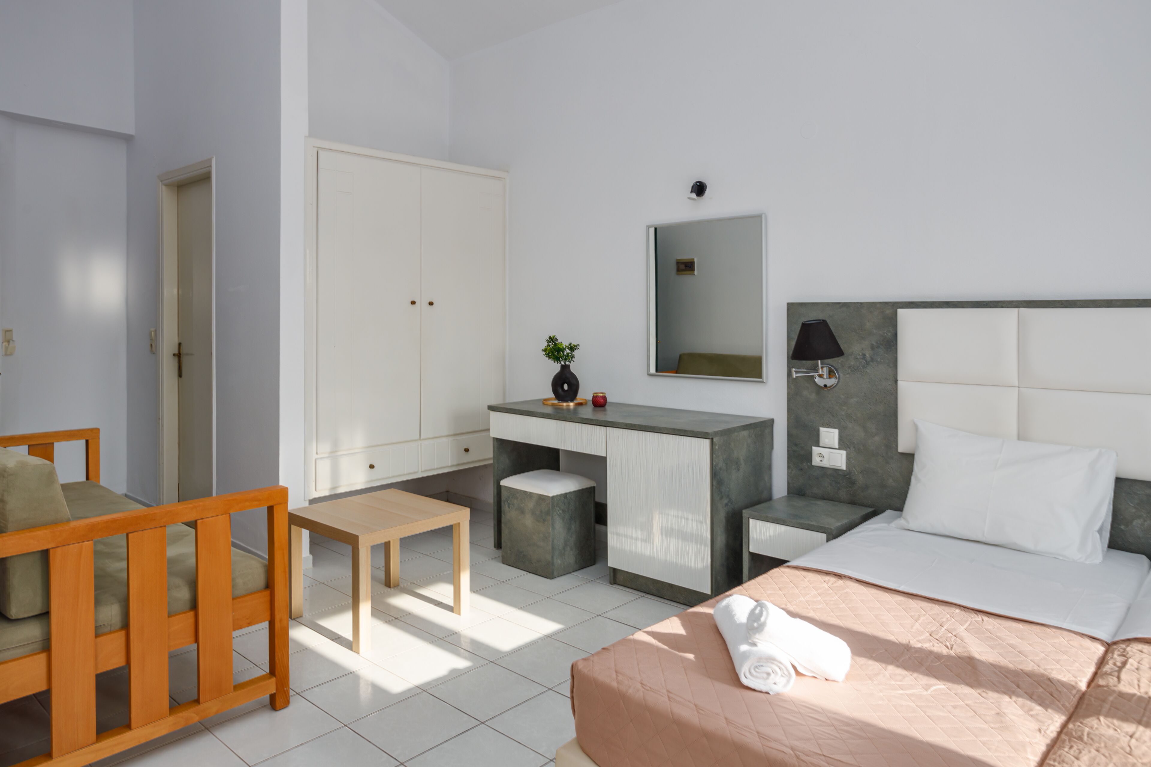 A hotel room with a bed, a desk, a chair, a wardrobe, and a mirror.
