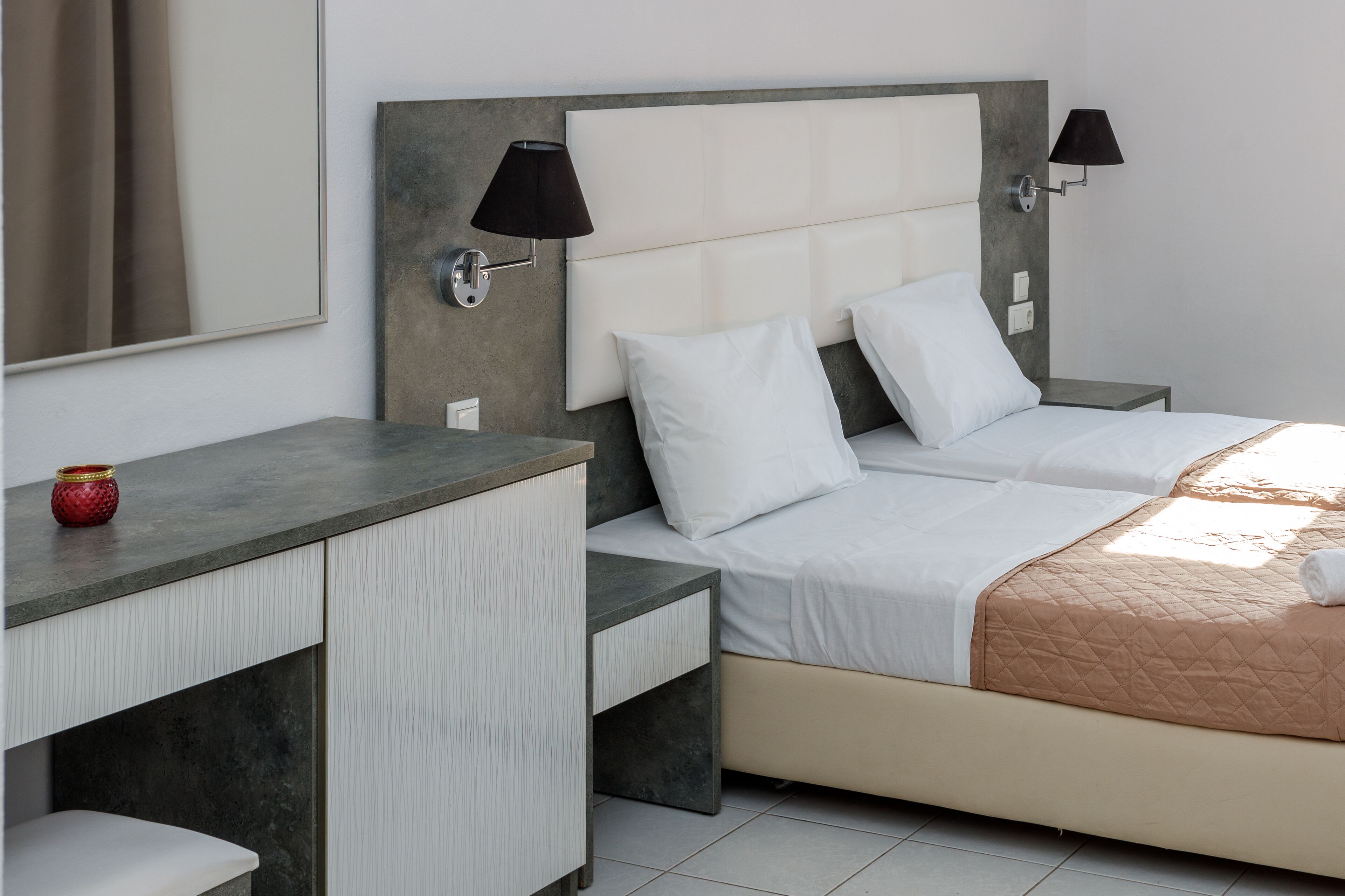A hotel room with two beds, a desk, and a mirror.