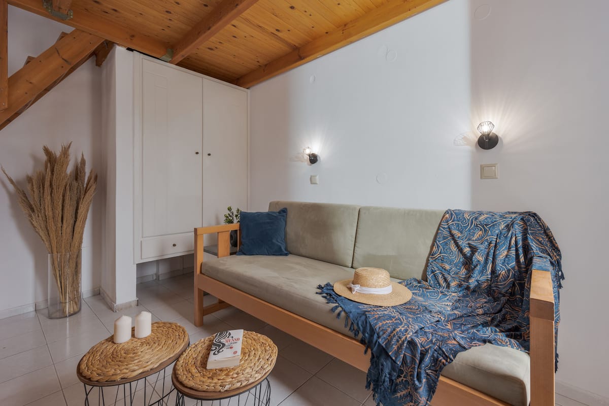 Una habitación acogedora con un banco de madera, un sofá y un jarrón grande con plantas secas.