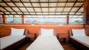 A room with three beds aligned in a row, wooden walls, and a ceiling with a grid pattern.