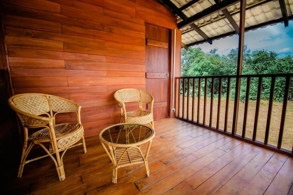 Un balcón de madera con dos sillones de mimbre y una mesa de vidrio.