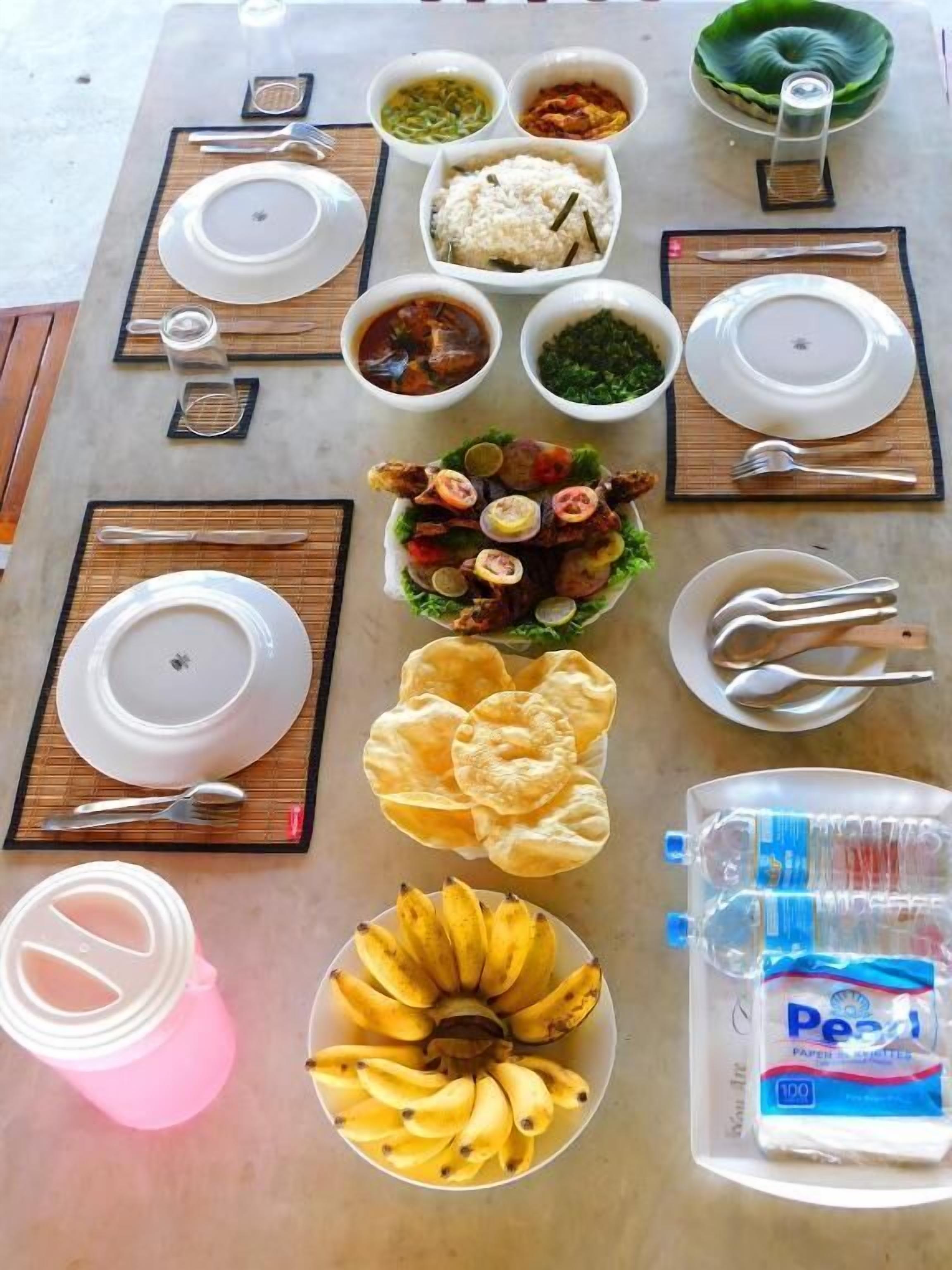 A table set with various dishes, including rice, soup, and a fish dish, along with utensils and a water bottle.