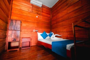 Una habitación de cabaña de madera con una cama, un mueble pequeño de madera, una mesita de noche y una litera.