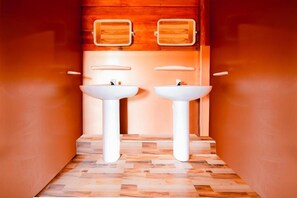 Un baño con dos lavamanos blancos, paneles de madera en la pared y suelo de baldosas.