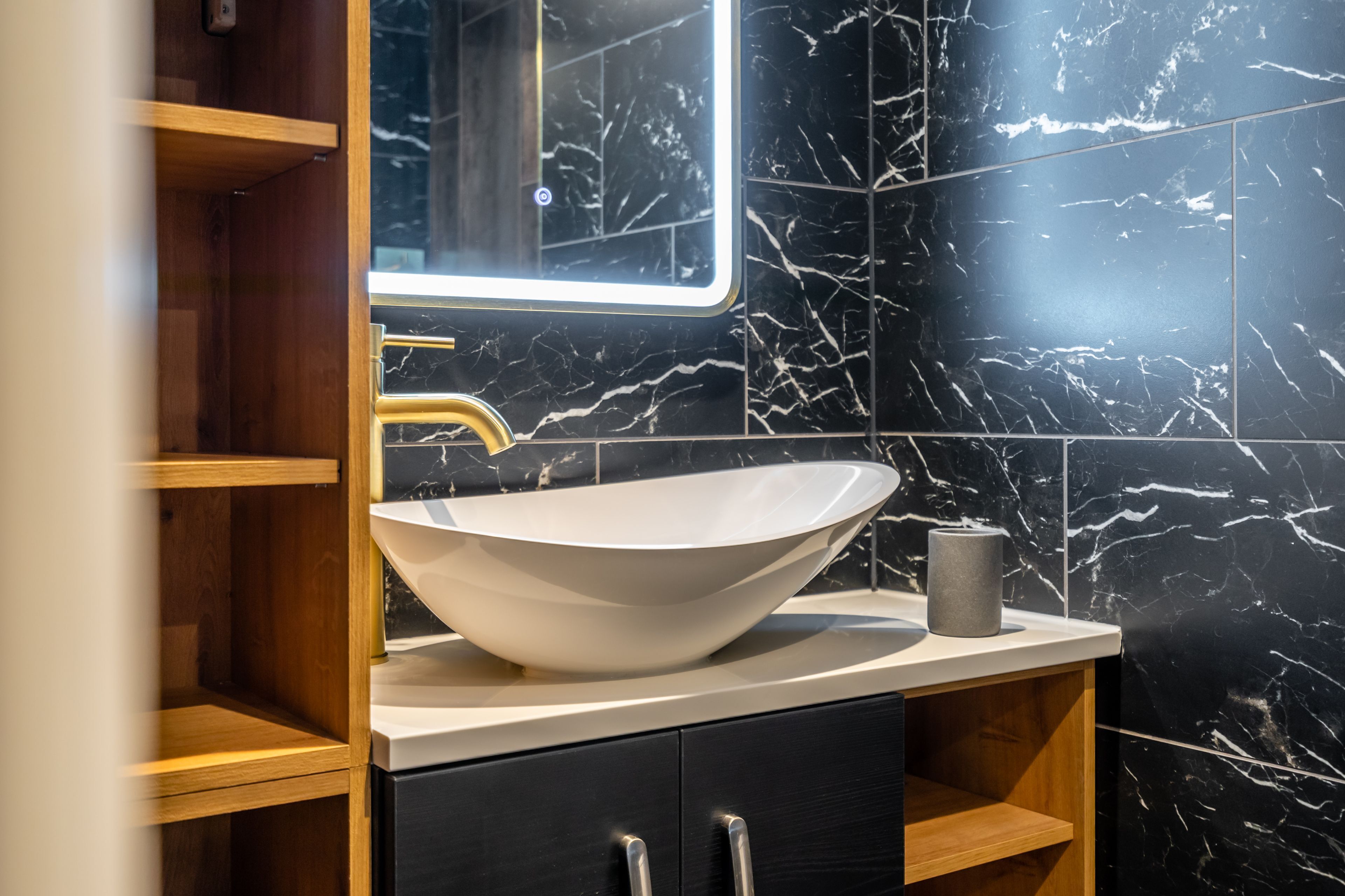 A bathroom with a white vessel sink, a mirror, and black marble walls.